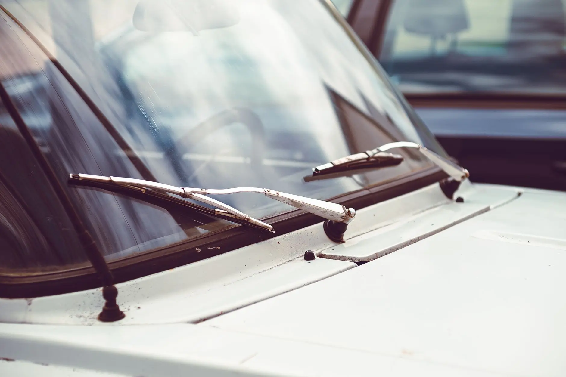 Detailed image of an old car windshield with rusty wipers and vintage appeal.